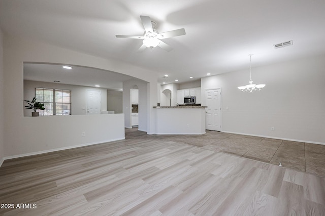 45633 W Mountain View Rd, Maricopa, AZ 85139 - unfurnished living room featuring visible vents, light wood-style floors, baseboards, arched walkways, and ceiling fan with notable chandelier