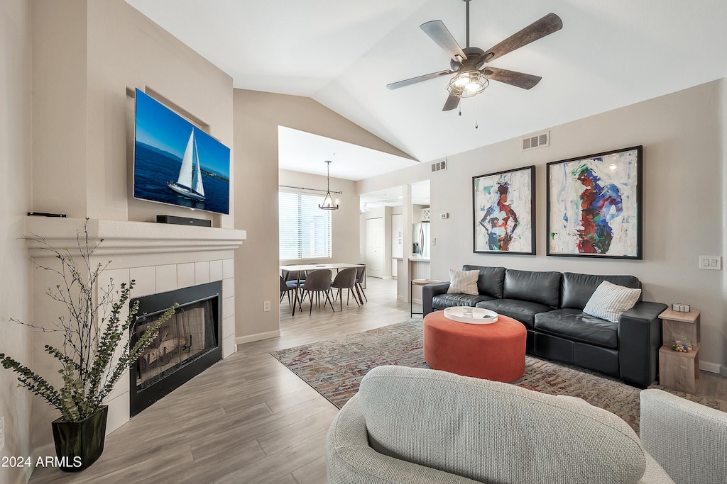 living room featuring vaulted ceiling, a tiled fireplace, light wood-type flooring, and ceiling fan with notable chandelier