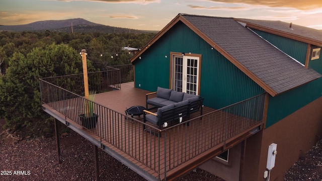 deck at dusk featuring a mountain view, french doors, and an outdoor living space