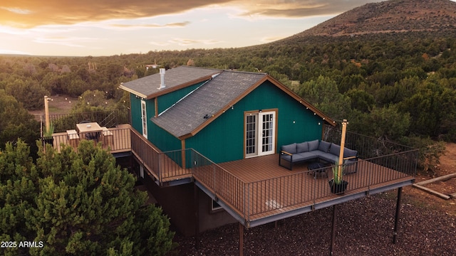 rear view of property featuring french doors, a wooden deck, a forest view, and an outdoor hangout area