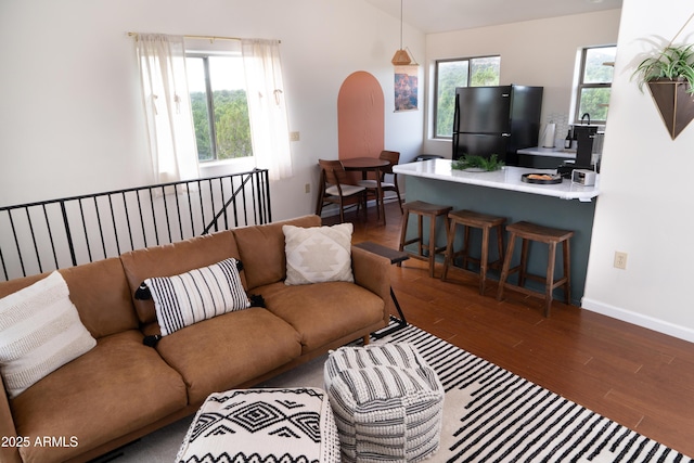 living room with dark wood-style floors, a wealth of natural light, arched walkways, and baseboards