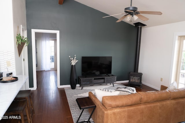 living area with ceiling fan, dark wood-type flooring, vaulted ceiling, and a wood stove