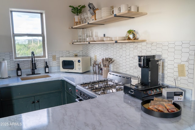 kitchen with white microwave, light stone counters, a sink, range, and open shelves