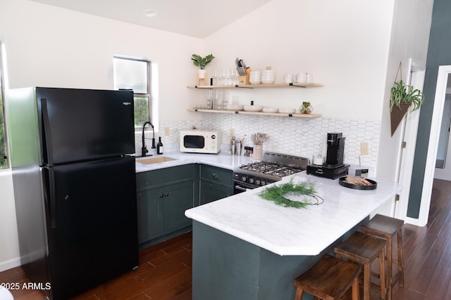 kitchen featuring stainless steel range, white microwave, freestanding refrigerator, open shelves, and a sink