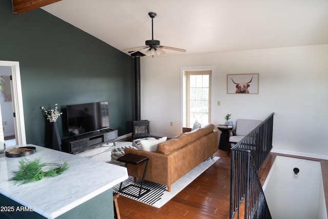 living room featuring a ceiling fan, a wood stove, vaulted ceiling, and dark wood-style flooring