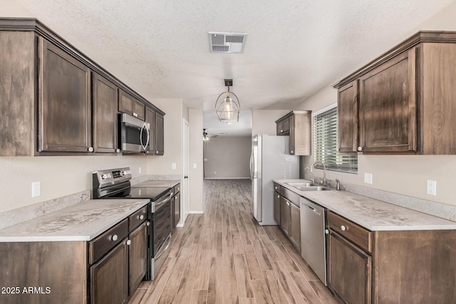 kitchen with appliances with stainless steel finishes, hanging light fixtures, dark brown cabinetry, a textured ceiling, and light hardwood / wood-style flooring