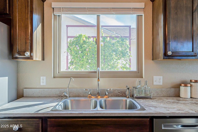 kitchen featuring dark brown cabinetry, sink, stainless steel dishwasher, and light stone countertops