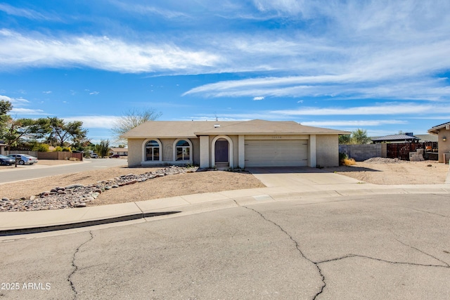 ranch-style home featuring concrete driveway, an attached garage, fence, and stucco siding