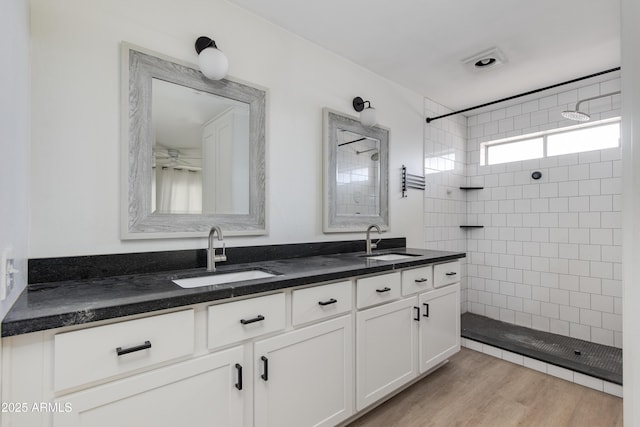 full bath featuring double vanity, walk in shower, a sink, and wood finished floors