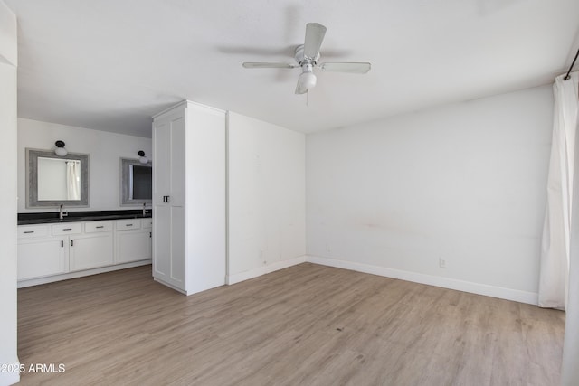 interior space with a ceiling fan, a sink, light wood-style flooring, and baseboards