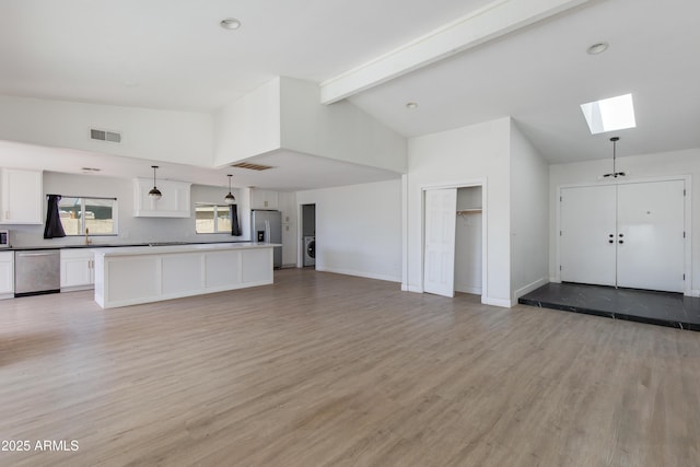 interior space with a skylight, appliances with stainless steel finishes, open floor plan, white cabinetry, and washer / dryer