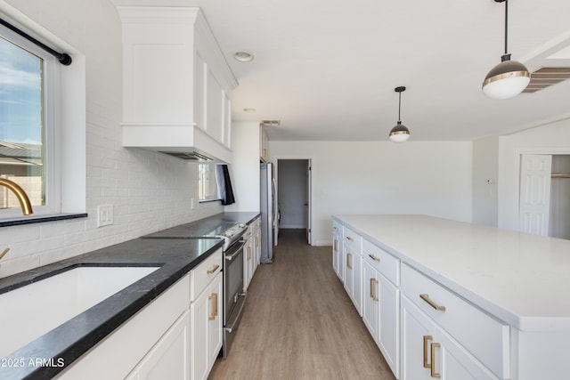 kitchen featuring light wood finished floors, decorative backsplash, custom range hood, stainless steel appliances, and a sink