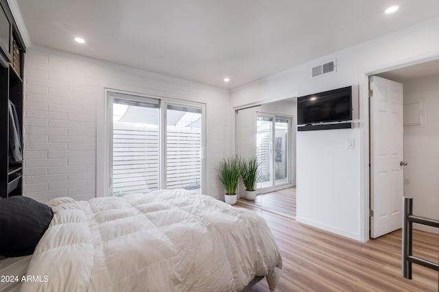 bedroom with light hardwood / wood-style floors, brick wall, access to outside, and a closet