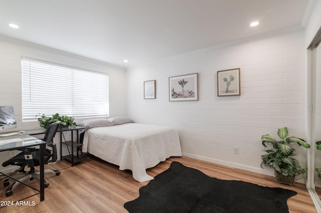 bedroom with light hardwood / wood-style floors, crown molding, and brick wall