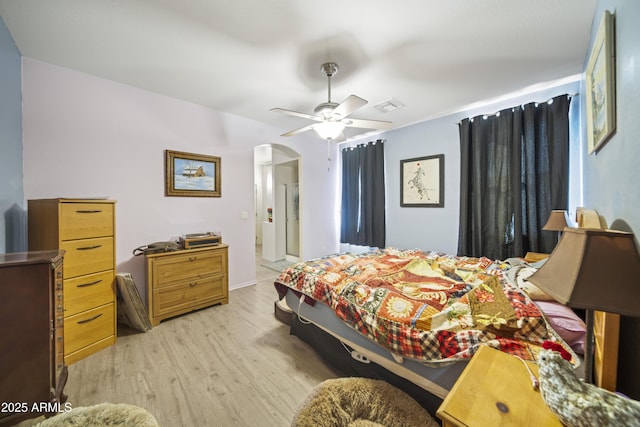 bedroom featuring arched walkways, visible vents, light wood-type flooring, and a ceiling fan