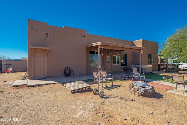 back of house with stucco siding, an outdoor fire pit, a hot tub, and fence