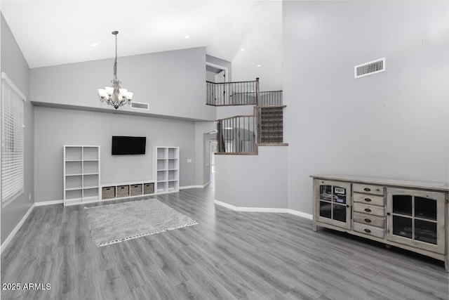 unfurnished living room featuring wood-type flooring, high vaulted ceiling, and a notable chandelier