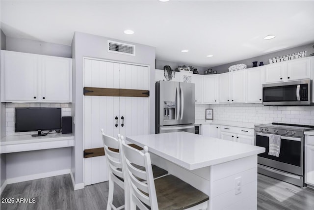 kitchen with dark wood-type flooring, appliances with stainless steel finishes, a kitchen island, and white cabinets