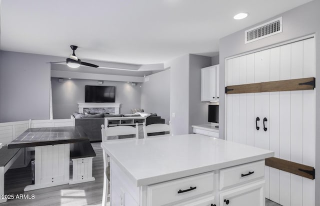 kitchen with light hardwood / wood-style flooring, ceiling fan, a kitchen breakfast bar, a center island, and white cabinets