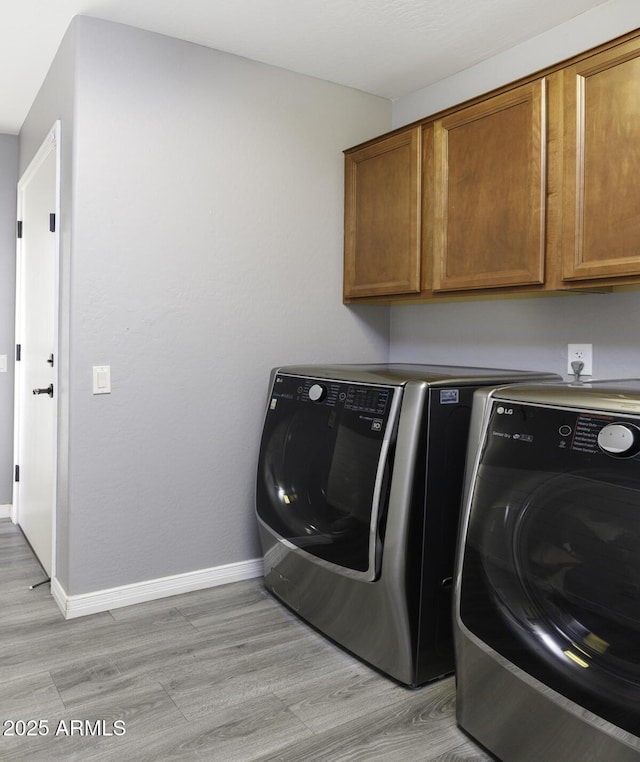 clothes washing area with light hardwood / wood-style flooring, washing machine and dryer, and cabinets