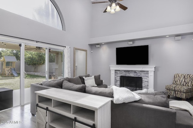 living room featuring a high ceiling, a stone fireplace, light wood-type flooring, and ceiling fan