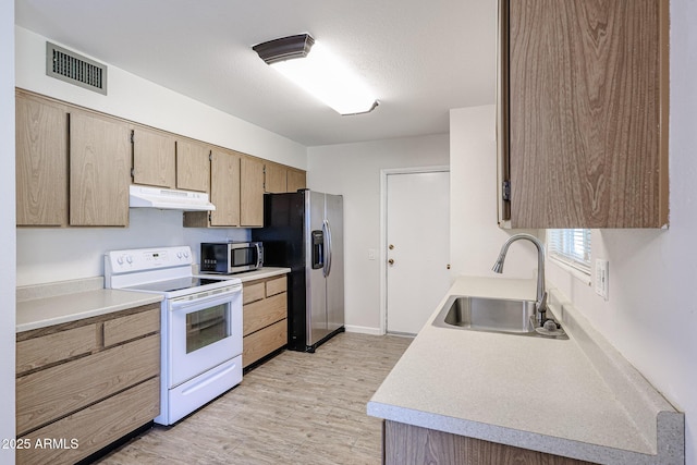 kitchen with appliances with stainless steel finishes, light brown cabinetry, sink, light hardwood / wood-style floors, and a textured ceiling