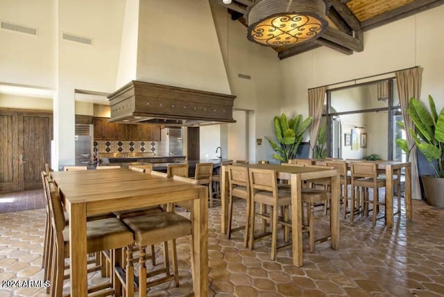 dining area featuring beam ceiling, a towering ceiling, and visible vents