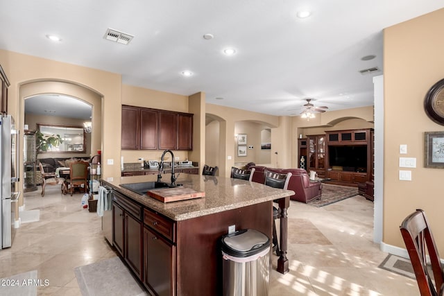 kitchen featuring appliances with stainless steel finishes, ceiling fan, sink, stone countertops, and a center island with sink