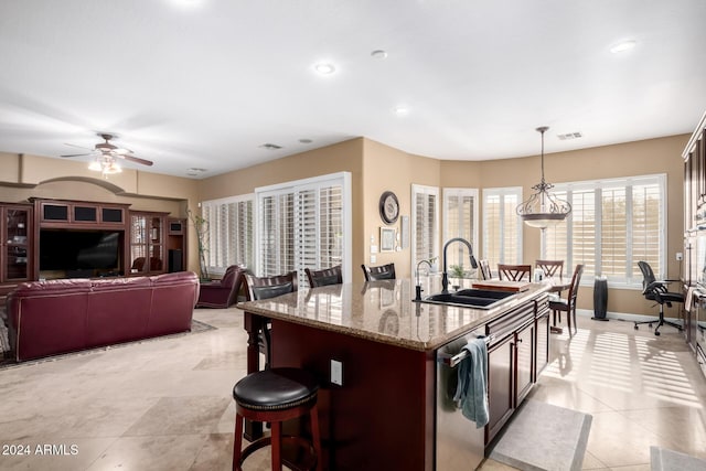 kitchen with sink, stainless steel dishwasher, pendant lighting, a breakfast bar area, and a center island with sink