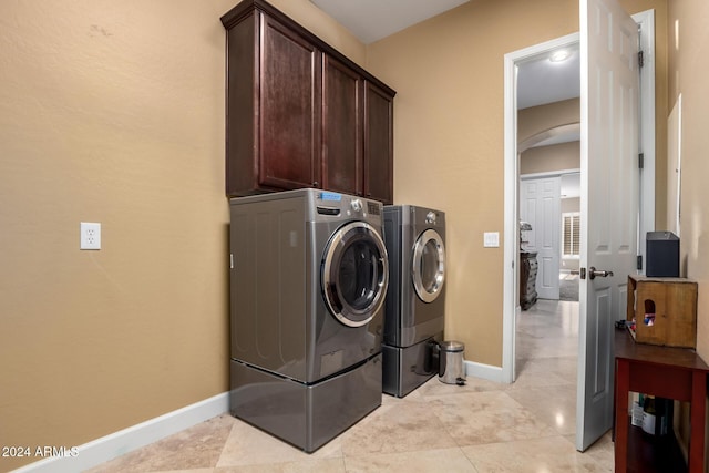 clothes washing area featuring cabinets, light tile patterned floors, and washing machine and clothes dryer