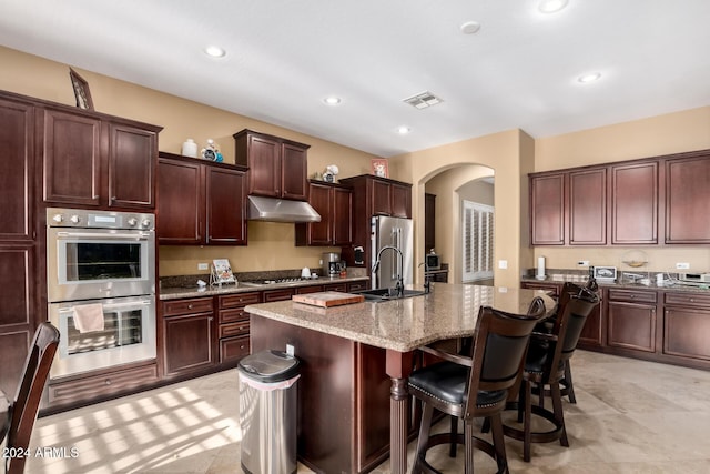 kitchen with appliances with stainless steel finishes, a kitchen breakfast bar, light stone counters, sink, and a center island with sink