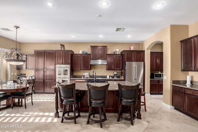 kitchen featuring light stone counters, an island with sink, pendant lighting, and appliances with stainless steel finishes