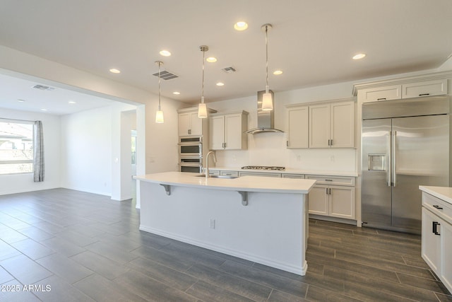 kitchen featuring a kitchen island with sink, wall chimney range hood, and stainless steel appliances