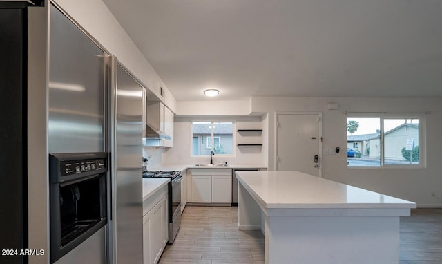 kitchen with light hardwood / wood-style flooring, sink, stainless steel appliances, a center island, and white cabinetry