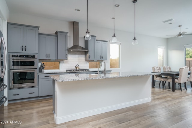 kitchen featuring appliances with stainless steel finishes, light stone counters, backsplash, and wall chimney exhaust hood