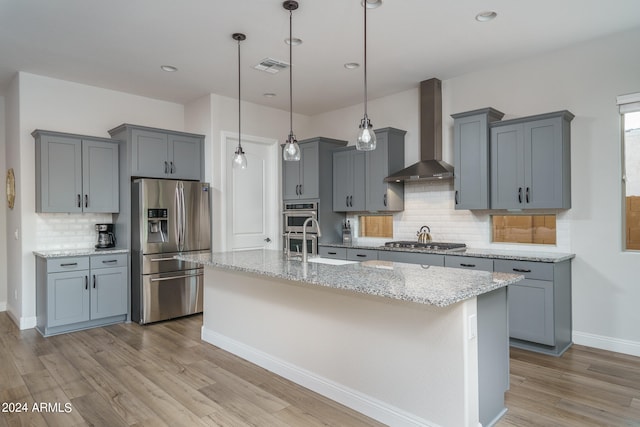 kitchen with stainless steel appliances, light stone counters, decorative backsplash, light wood-type flooring, and wall chimney exhaust hood