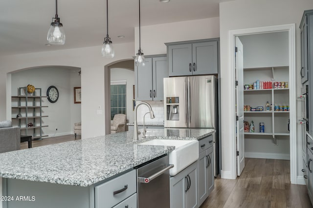 kitchen featuring tasteful backsplash, stainless steel appliances, light stone counters, an island with sink, and wood-type flooring