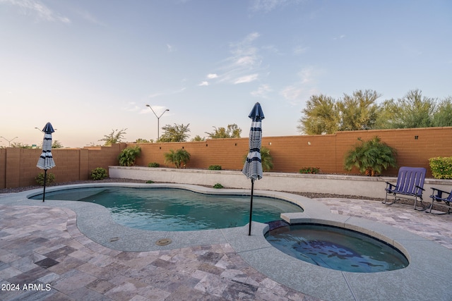 pool at dusk with an in ground hot tub and a patio area