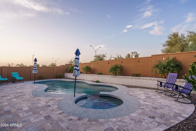 pool at dusk featuring an in ground hot tub and a patio area