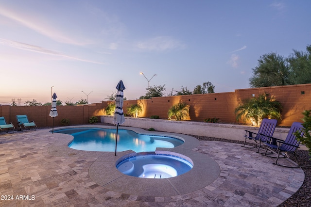 pool at dusk featuring an in ground hot tub and a patio