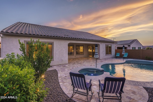 back house at dusk with a pool with hot tub, a patio area, and solar panels