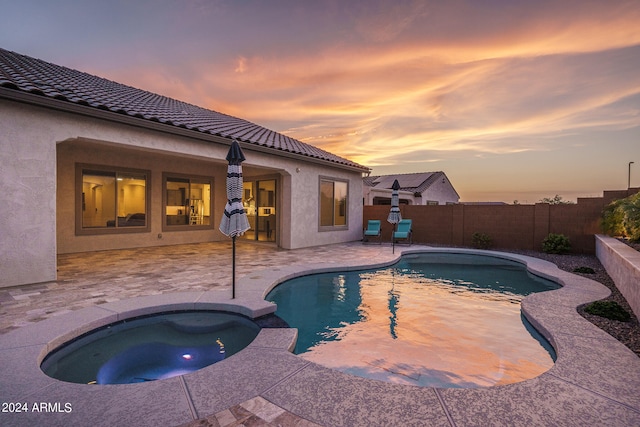 pool at dusk with an in ground hot tub and a patio area