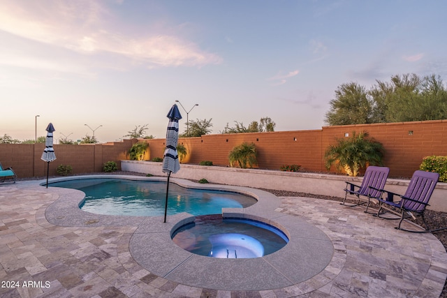 pool at dusk with an in ground hot tub and a patio