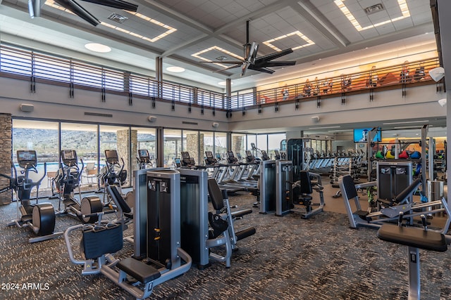 exercise room with carpet floors, coffered ceiling, ceiling fan, and a high ceiling