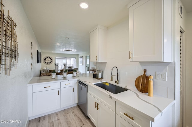 kitchen with white cabinetry, a sink, stainless steel dishwasher, tasteful backsplash, and light wood-type flooring