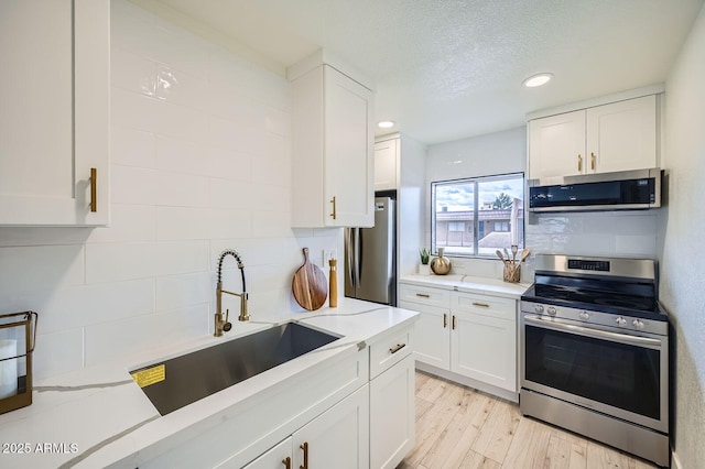 kitchen with a sink, tasteful backsplash, white cabinetry, light wood-style floors, and appliances with stainless steel finishes