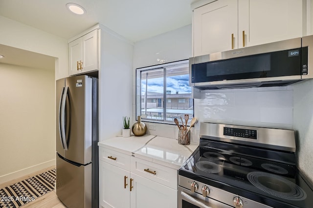 kitchen featuring light stone counters, white cabinetry, appliances with stainless steel finishes, decorative backsplash, and baseboards