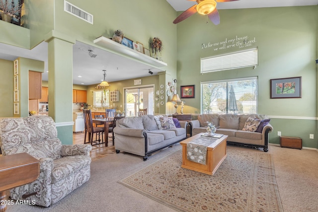 living area featuring light carpet, a towering ceiling, visible vents, and a wealth of natural light