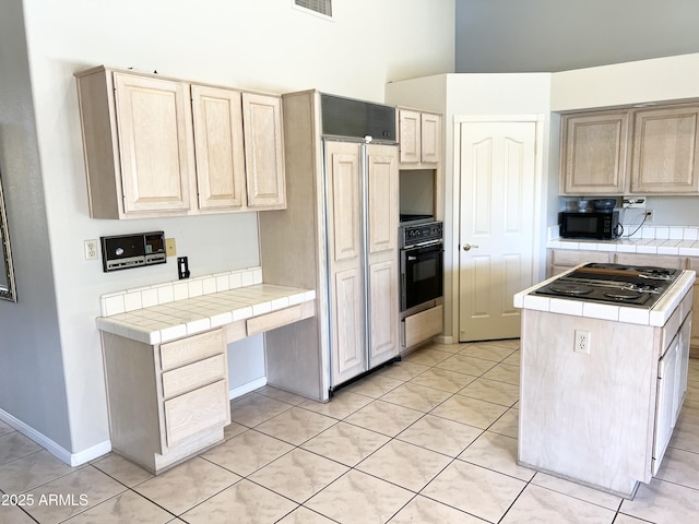 kitchen featuring black appliances, tile counters, light tile patterned flooring, and light brown cabinetry