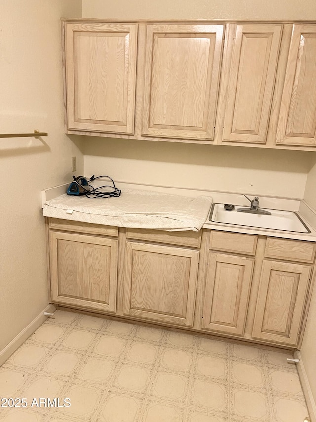 clothes washing area with light floors, baseboards, and a sink